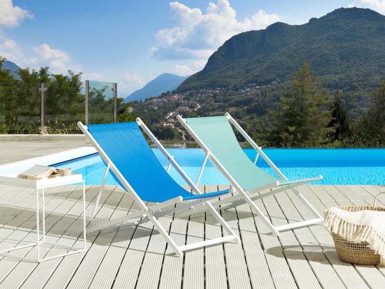 Zwei Liegestühle aus Stoff und Holz am Pool mit Berglandschaft im Hintergrund.