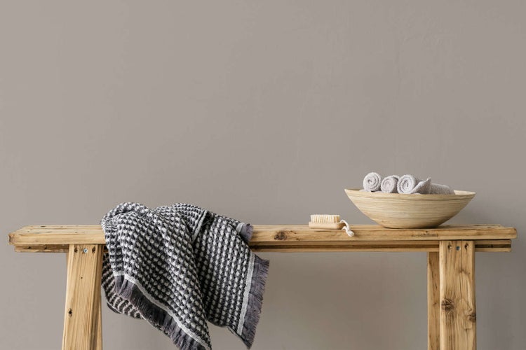Organisierte Badezimmerszene mit matter Wandfarbe, rustikaler Holzbank, kariertem Handtuch und einer Holzschale mit Gästehandtüchern.