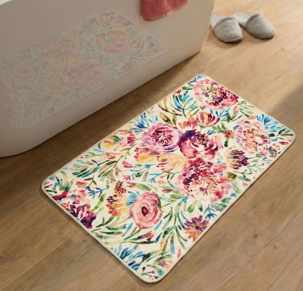 Rechteckige Badematte mit farbenfrohem Blumenmuster auf einem Holzboden neben einer Badewanne in einem hellen Badezimmer.