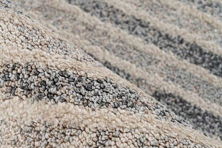 Nahaufnahme eines Teppichs mit strukturierter Oberfläche und wellenförmigem Streifenmuster in Beige und Grau.