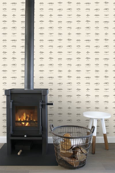 Innenraum mit Kaminofen, Holzkohlekorb mit Brennholz und Hocker vor einer Tapete mit Knotenmotiven