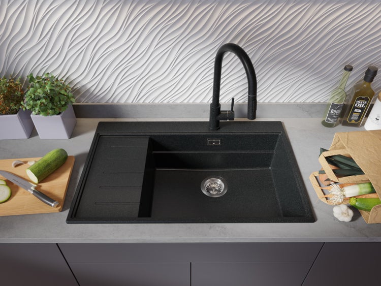 Schwarzes Spülbecken mit Abtropffläche und schwarzer Armatur auf einer Küchentheke mit Gemüse