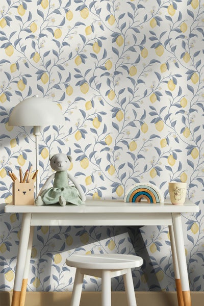 Kinderzimmer mit Schreibtisch, Hocker, Lampe und Zubehör vor einer Tapete mit Zitronenmuster.