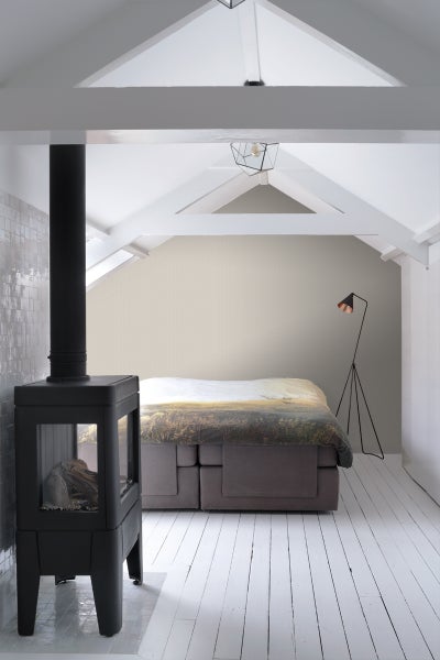 Schlafzimmer mit Kaminofen, Bett und Stehlampe auf einem Dachboden mit Holzbalken