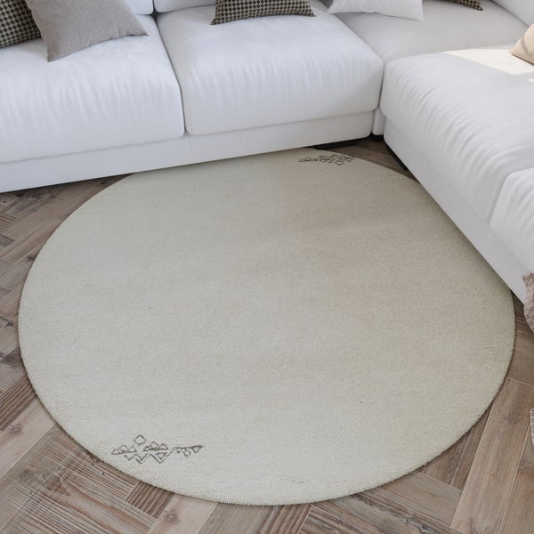 Runder, weicher Teppich mit dezentem Muster auf Holzfußboden in einem hellen, modern eingerichteten Wohnzimmer mit weißem Sofa.