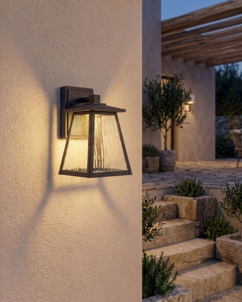 Moderne Außenwandleuchte mit strukturiertem Glas an einer Hauswand, beleuchteter Außenbereich mit Steintreppe und Pflanzen im Hintergrund.