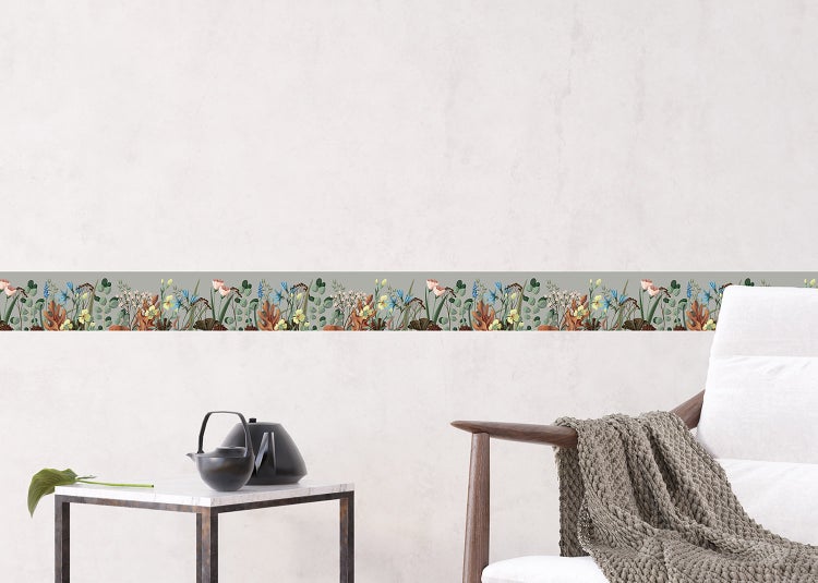 Tapetenbordüre mit Wiesenblumen-Motiv in einem hellen Wohnzimmer mit beigem Sofa und Holzmöbeln auf einem Teppich.