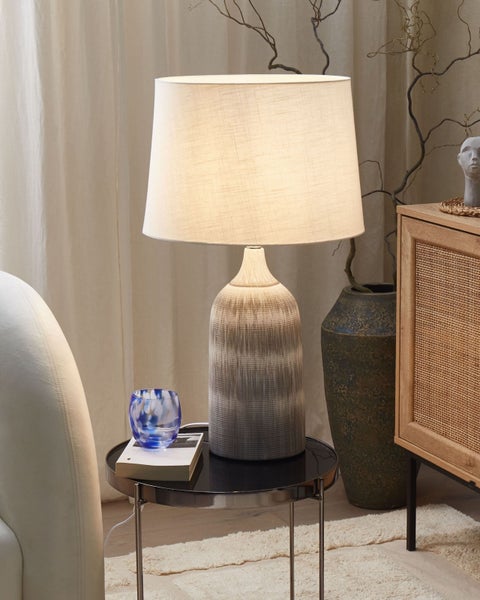 Dekorative Tischleuchte mit Stoffschirm auf einem Beistelltisch in einem Wohnzimmer.