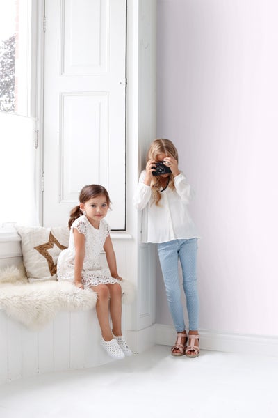 Zwei Mädchen in einem hellen Raum: eines sitzt auf einer Bank mit Kissen, das andere macht Fotos