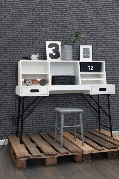 Weißer Schreibtisch mit Schubladen, Ablageflächen und schwarzem Metallgestell vor einer gemusterten Tapete