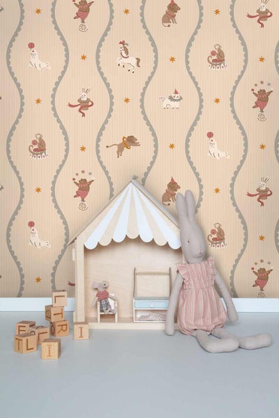 Kindertapete mit Zirkusmotiven wie Bären, Affen und Robben in vertikalen Wellenlinien, davor ein Holzpuppenhaus und ein Stoffhase im Kinderzimmer.