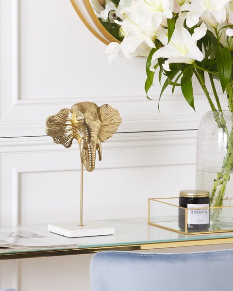 Dekorative goldfarbene Elefantenskulptur auf einem Tisch neben einer Duftkerze und Blumen in einer Vase