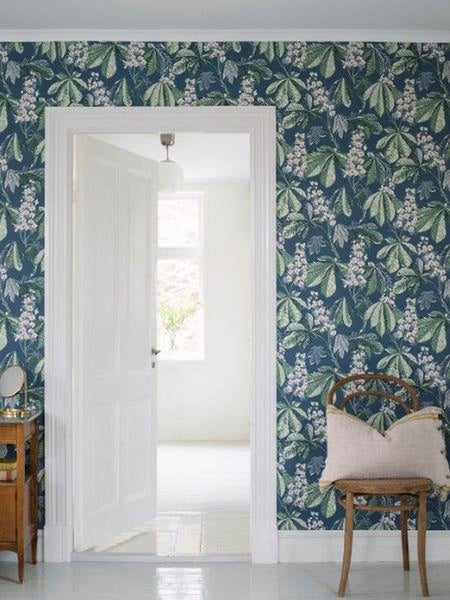 Schlafzimmer mit floraler Tapete, Rattanbett und Nachttisch mit Zimmerpflanzen