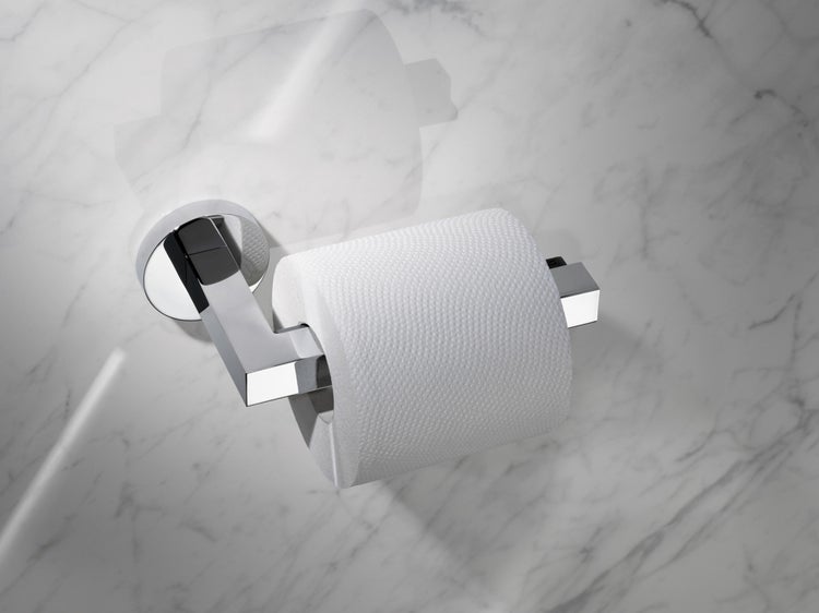 Wandmontierter Toilettenpapierhalter aus Metall mit glänzender Oberfläche inklusive einer Rolle Toilettenpapier vor einer Marmorwand.