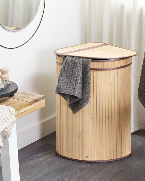 Eckiger Wäschekorb aus Bambus mit Deckel im Badezimmer, ein graues Handtuch hängt über dem Rand.