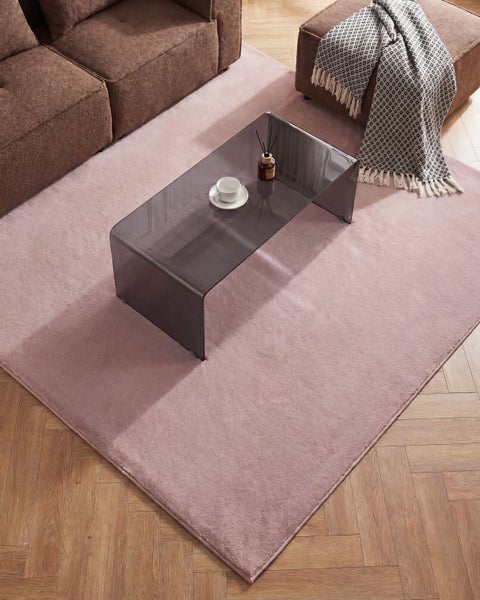 Rechteckiger, flauschiger Teppich in einem modernen Wohnzimmer mit braunem Sofa, Glastisch aus dunklem Glas und Fischgrätenparkett.