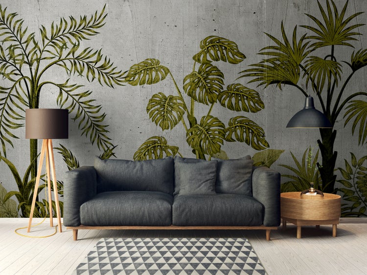 Modernes Wohnzimmer mit grüner Dschungel-Fototapete auf Betonoptik-Wand, dunkelgrauem Sofa, Dreibein-Stehleuchte und geometrischem Teppich.