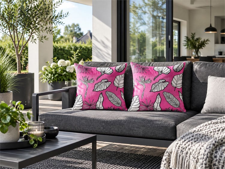 Zwei Zierkissen mit Blumenmuster auf einem dunklen Loungesofa auf einer Terrasse mit Garten im Hintergrund.