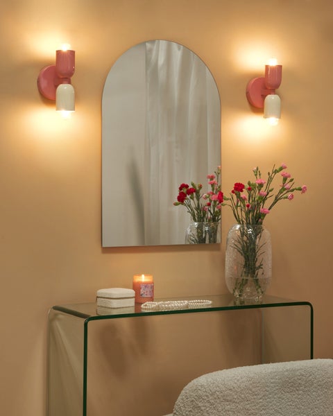 Arrangement mit einem Spiegel, zwei Wandleuchten, einer Glasablage und dekorativen Elementen.