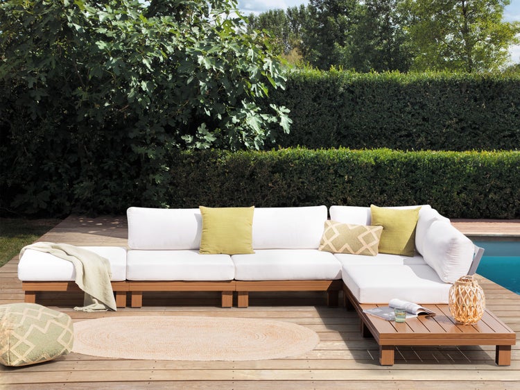 Gartenszene mit modularem Sofa, Beistelltisch, Pouf und rundem Teppich auf einer Holzterrasse