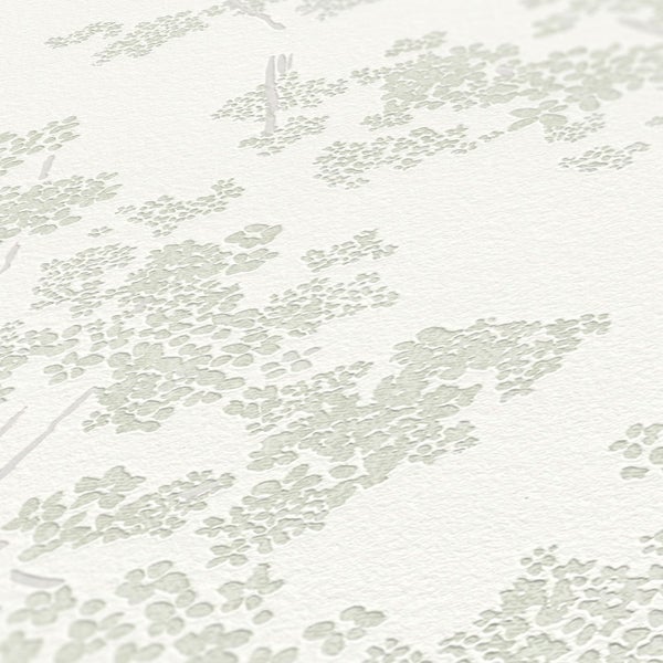 Nahaufnahme eines dekorierten Zimmers mit einer floral gemusterten Tapete und dekorativen Objekten auf einer dunklen Holzkommode.