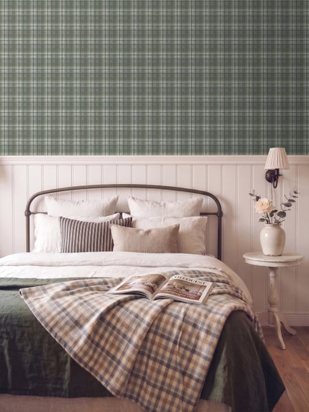 Schlafzimmer mit grün-weiß karierter Vliestapete im Landhausstil über weißer Wandtäfelung, Metallbett und Nachttisch.
