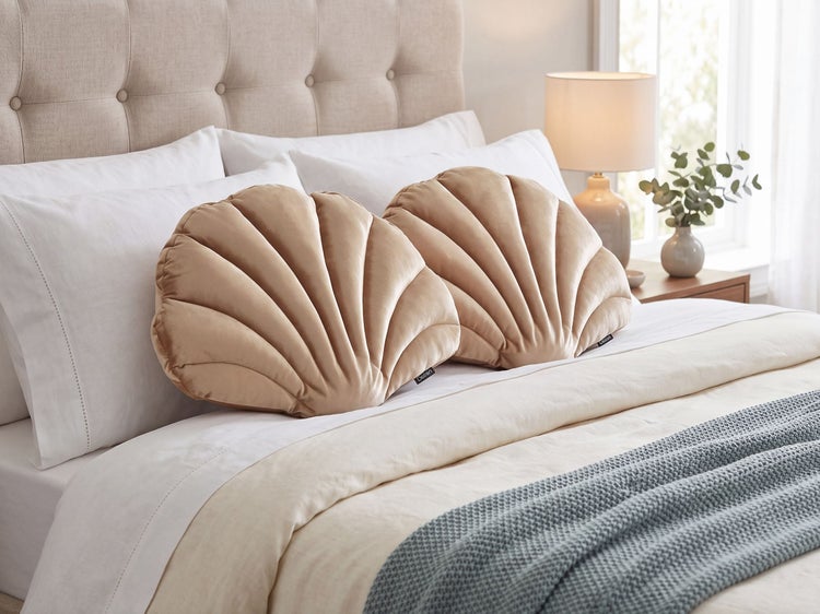 Zwei muschelförmige Zierkissen aus Samtstoff auf einem bequemen Schlafzimmerbett mit gestepptem Kopfteil und gemütlicher Ausstattung.
