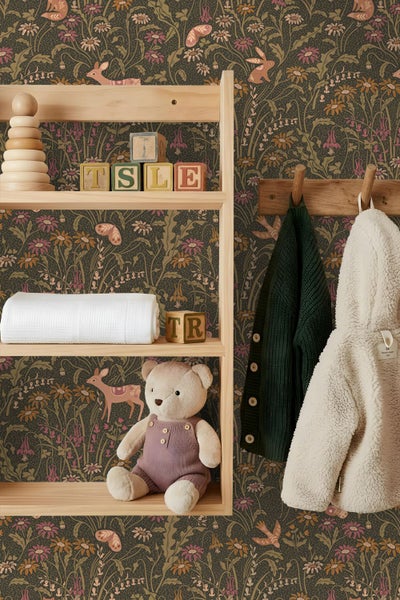 Tapete mit Tiermotiv und Blumen in einem Kinderzimmer hinter einem Holzregal mit Spielzeug und einer Wandgarderobe mit Jacken.