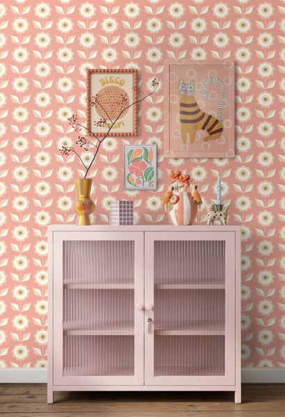 Vliestapete im Retrostil mit floralem Muster in Rosa und Weiß hinter einem rosa Metallschrank mit Riffelglas-Türen.