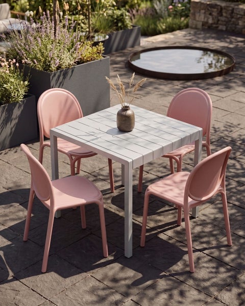 Modernes Gartenmöbel-Set mit einem quadratischen grauen Tisch und vier rosa Kunststoffstühlen auf einer Steinterrasse.