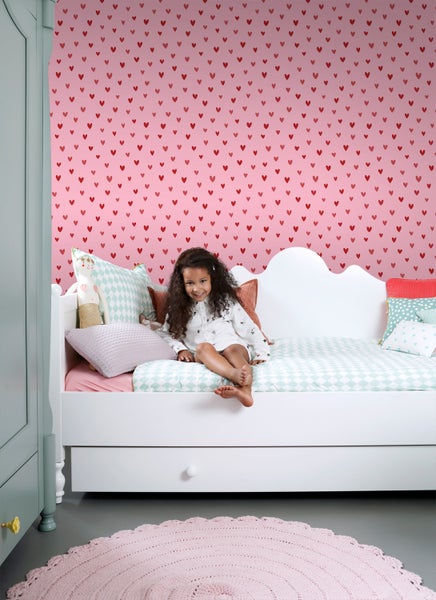 Mädchenzimmer mit Herzchen Tapete, weißem Bett, Schrank und rundem Teppich