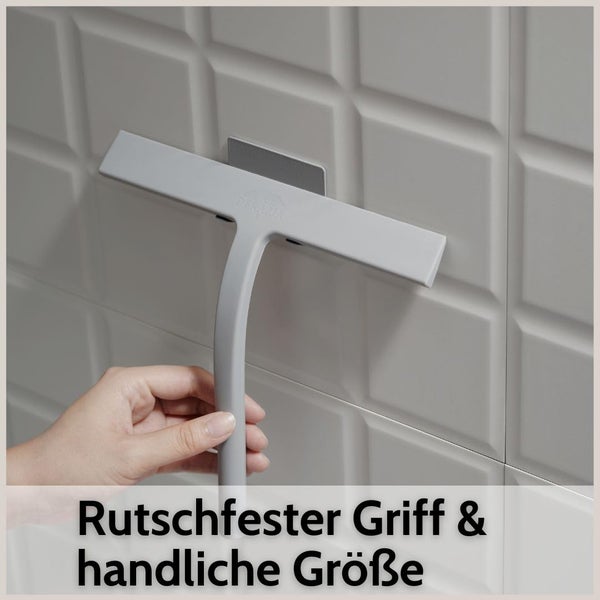 Hand hält einen Duschabzieher mit rutschfestem Griff und handlicher Größe an einer Wandhalterung vor Fliesen.