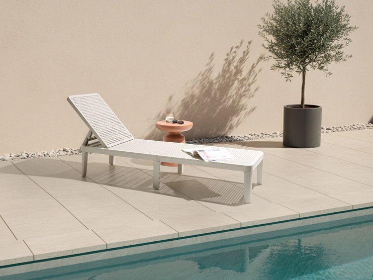 Gartenszene mit einer verstellbaren Liege, einem Beistelltisch und einer Topfpflanze neben einem Pool.