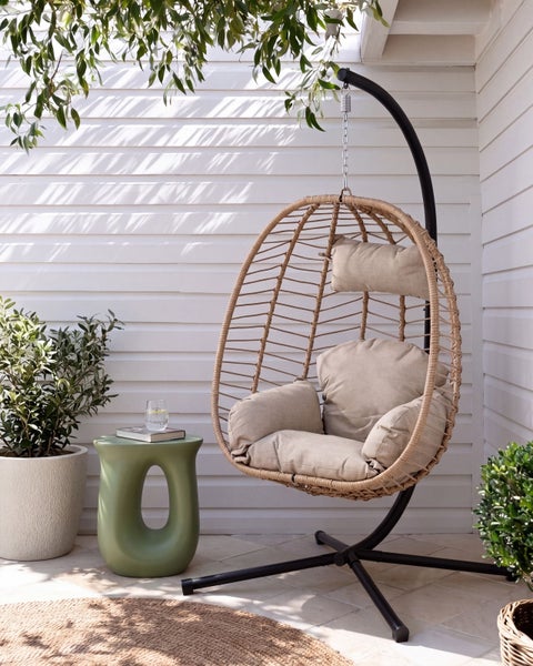 Hängesessel in Ei-Form mit weichen Kissen und Metallgestell auf einer Terrasse mit Beistelltisch und Pflanzen