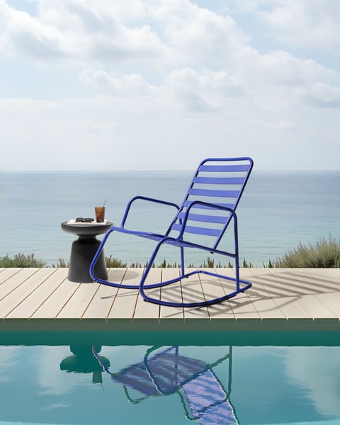 Szene mit einem blauen Schaukelstuhl aus Metall auf einer Holzterrasse neben einem Pool mit Meerblick