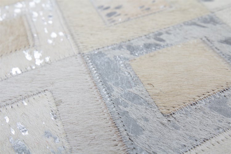 Detailansicht eines Patchwork-Teppichs aus echtem Kuhfell mit sichtbaren Naehten und silbernen Metallic-Akzenten.