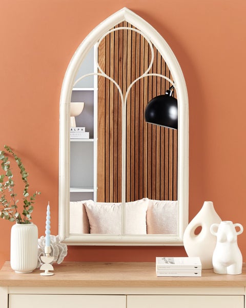 Dekorative Szene mit Spiegel in Kirchenfensterform, Vasen und Kerzen auf einem Holzschrank