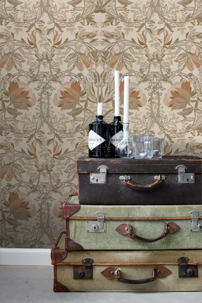 Dekorative Szene mit Stapel alter Koffer, Flaschen und Kerzen vor einer floralen Tapete.