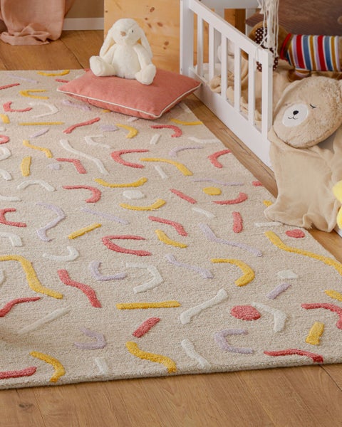 Hochflor-Kinderteppich mit abstraktem Wellenmuster in einem hellen Kinderzimmer neben einem weißen Holzbett und Kuscheltieren.