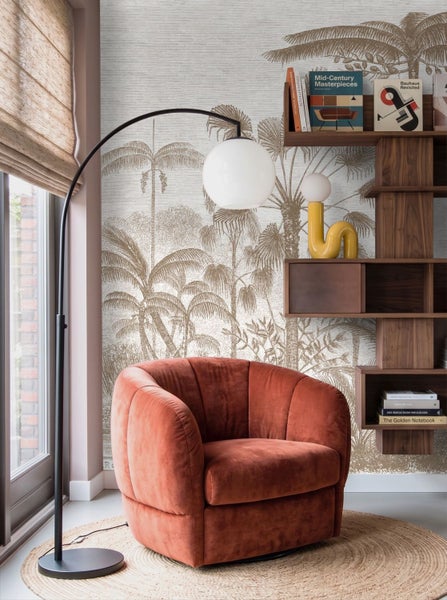 Modernes Wohnzimmer mit orangefarbenem Samtsessel, schwarzer Bogenlampe, Holzregal und Vliestapete mit braunem Palmenmuster im Skizzenstil.