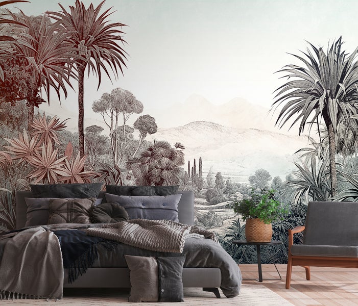 Schlafzimmer mit großflächiger Fototapete mit Tropenlandschaft, Palmen und Bergen, grauem Polsterbett und grauem Sessel.