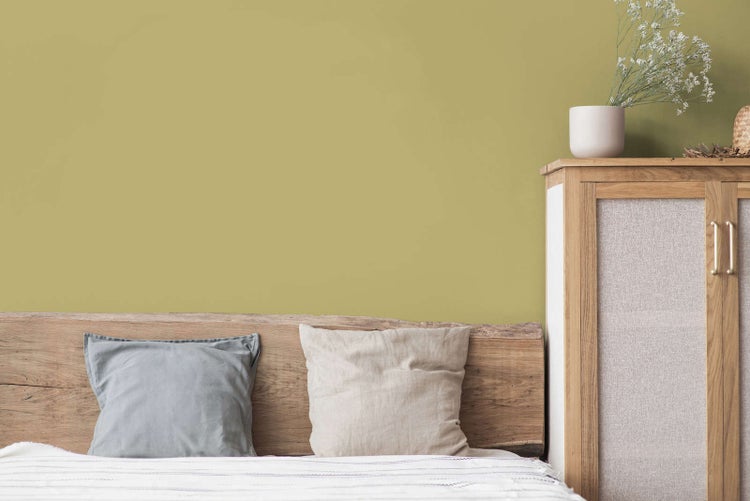 Schlafzimmer mit olivgrüner Wand, Kopfteil aus Naturholz, Kissen und Holzschrank mit weißen Blumen in hellem, organisiertem Ambiente.