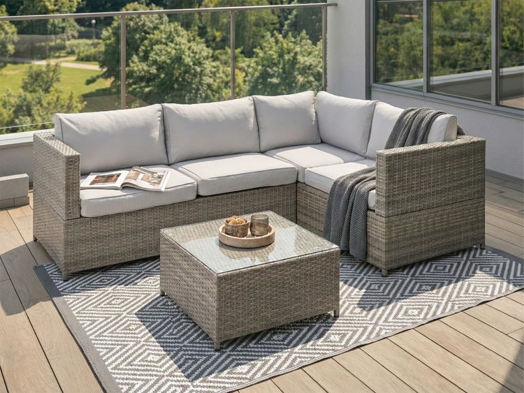 Terrasse mit Rattan-Lounge-Ecke, Couchtisch mit Glasplatte und Teppich mit grafischem Muster