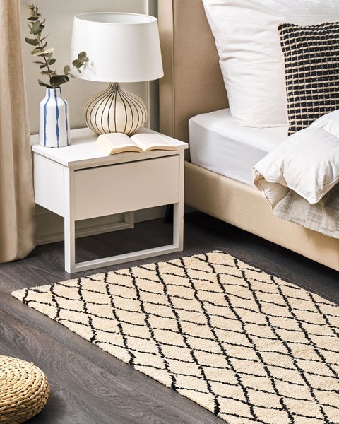 Schlafzimmer mit Bett, Nachttisch und Teppich mit Rautenmuster