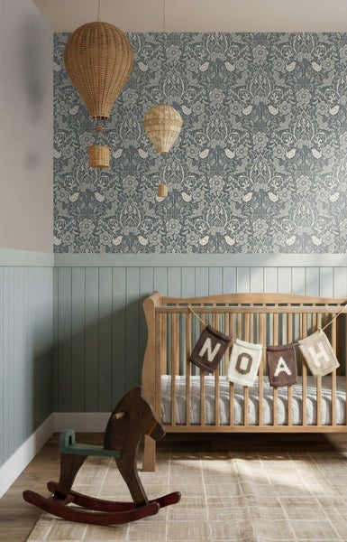 Hell gestaltetes Kinderzimmer mit floral gemusterter Tapete, grüner Holzvertäfelung, Holz-Kinderbett, Schaukelpferd und dekorativen Heißluftballons.