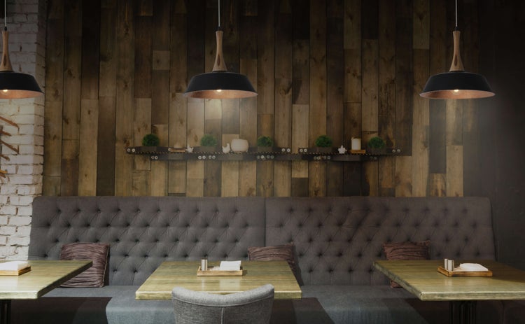 Restaurantinnenraum mit Holzwand, gepolsterter Sitzbank, Tischen und Pendelleuchten