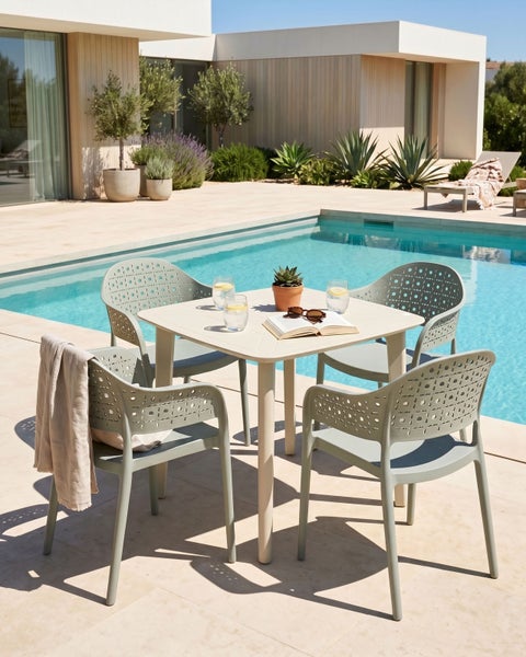 Modernes Gartenmöbel-Set mit quadratischem Tisch und vier Kunststoffstühlen auf einer hellen Terrasse an einem Pool.