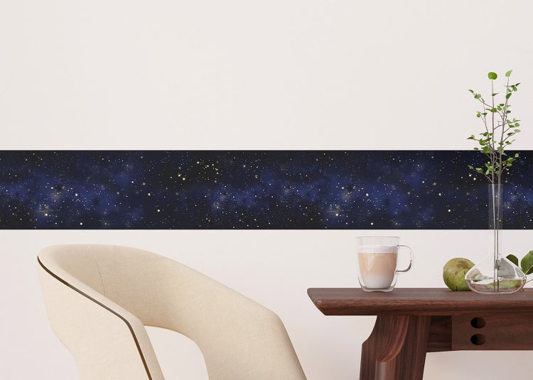 Selbstklebende Wandbordüre mit Sternenhimmel-Muster an einer weißen Wand hinter einem Sofa mit Kissen.