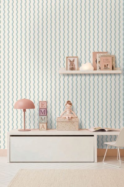 Helles und organisiertes Kinderzimmer mit Tapete mit vertikalen Wellenlinien, einem weißen Schreibtisch, einem Wandregal und einer rosa Tischlampe.