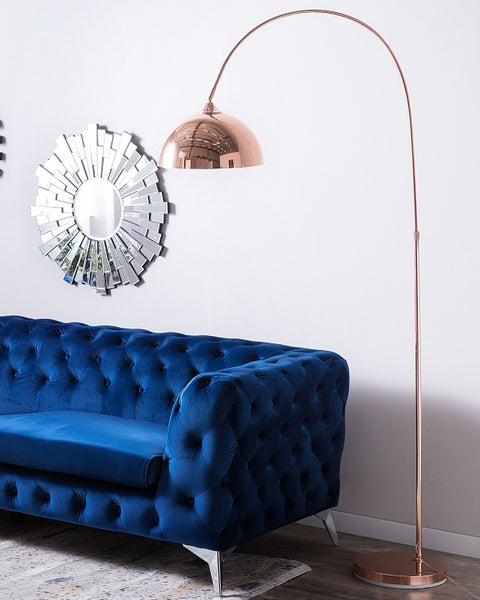 Szene mit einem blauen Sofa, einem Spiegel mit Sonnenstrahlenmuster und einer Stehlampe mit Bogen